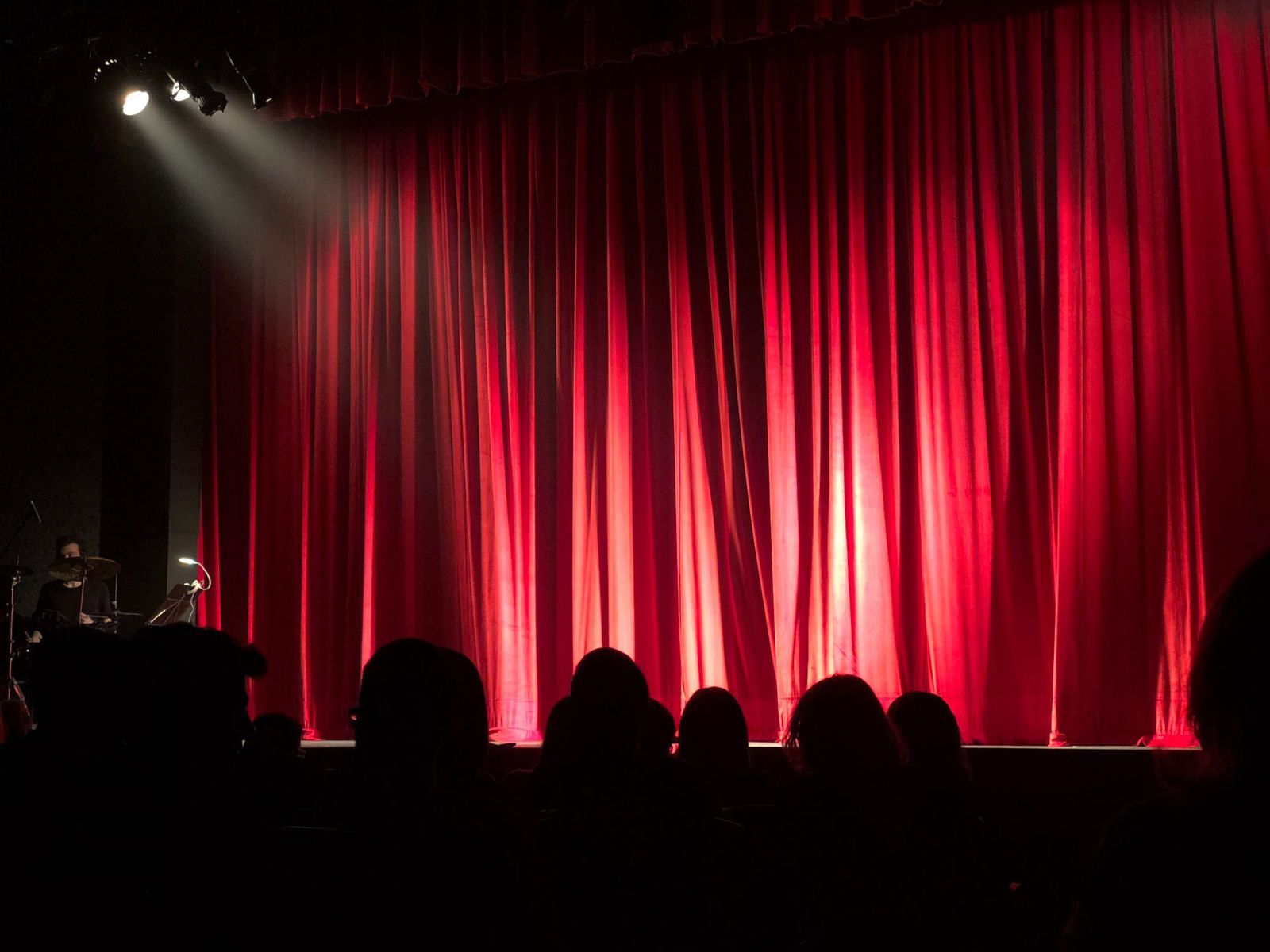 A theatre stage with red curtains and an audience in silhouette