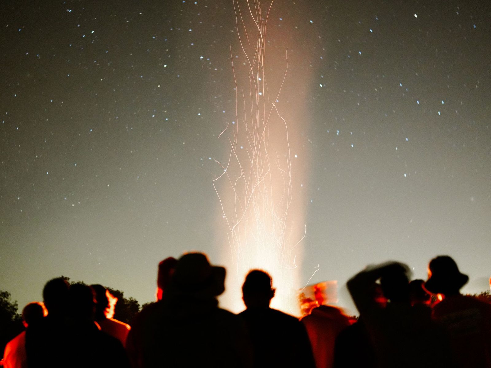 Friends silhouetted around a bonfire under a starry sky