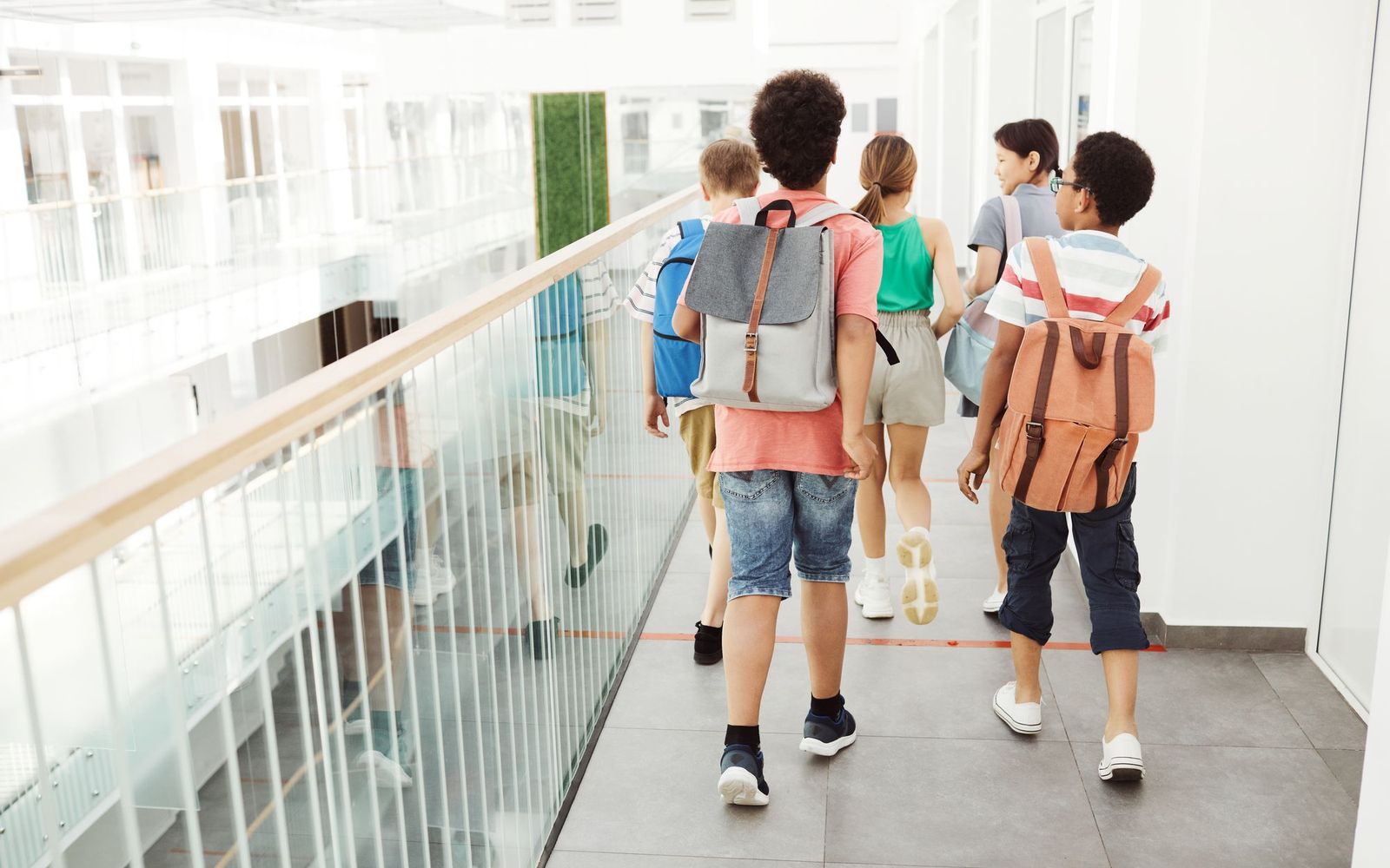 Students with backpacks walking along a bright school corridor, seen from behind
